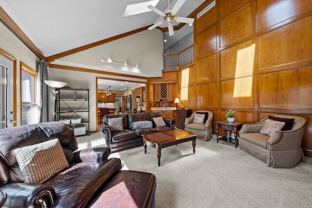 carpeted living room featuring a decorative wall, high vaulted ceiling, wood walls, and ceiling fan