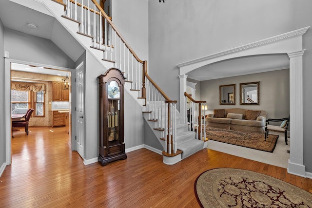 entrance foyer with stairway, baseboards, decorative columns, light wood-style floors, and a towering ceiling