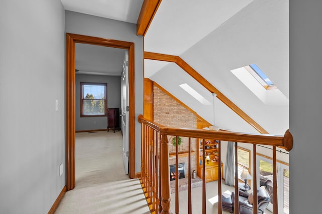 corridor with lofted ceiling with skylight, baseboards, and light carpet