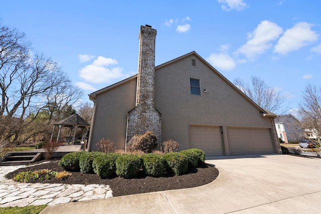 view of home's exterior with a gazebo, stucco siding, driveway, and a chimney