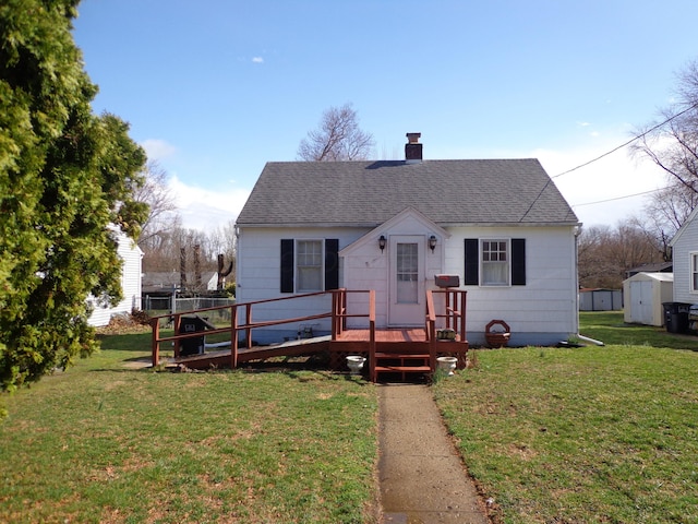 bungalow-style home with a front lawn, a wooden deck, roof with shingles, an outdoor structure, and a storage unit