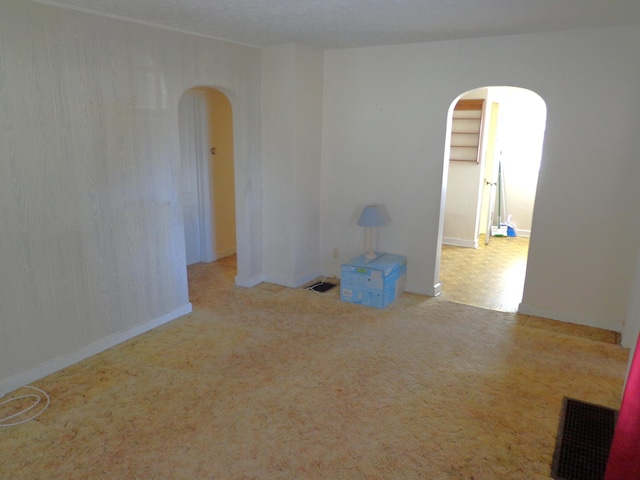 empty room featuring visible vents, arched walkways, and carpet floors