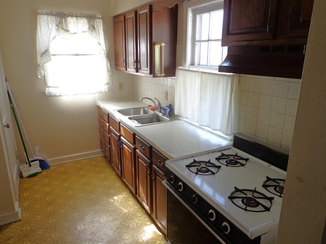 kitchen with light floors, a sink, gas range oven, under cabinet range hood, and backsplash