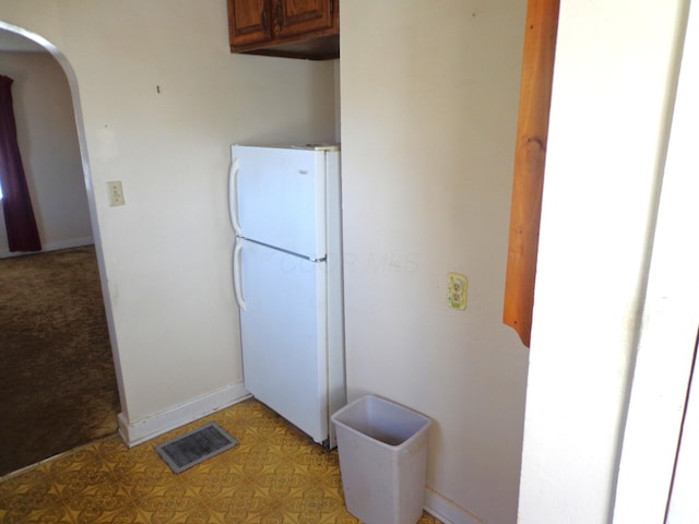 kitchen with visible vents, brown cabinetry, baseboards, freestanding refrigerator, and arched walkways