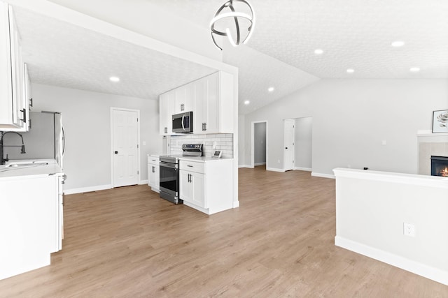 kitchen with open floor plan, a fireplace, white cabinets, stainless steel appliances, and a sink
