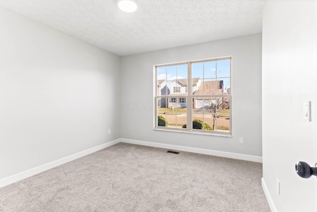 carpeted spare room featuring visible vents, baseboards, and a textured ceiling