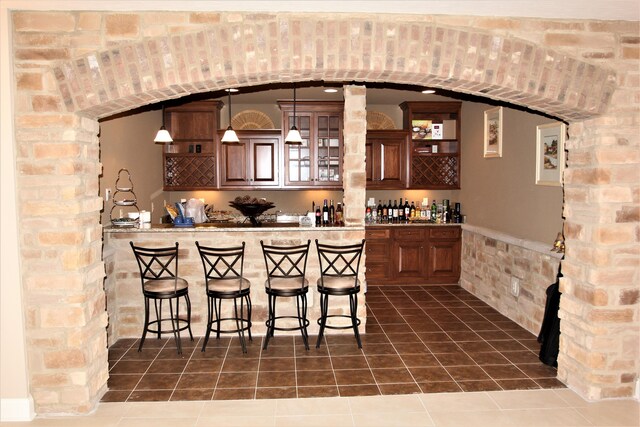 6884 Ballantrae Pl, Dublin, OH 43016 - bar featuring wet bar, dark tile patterned flooring, arched walkways, and hanging light fixtures