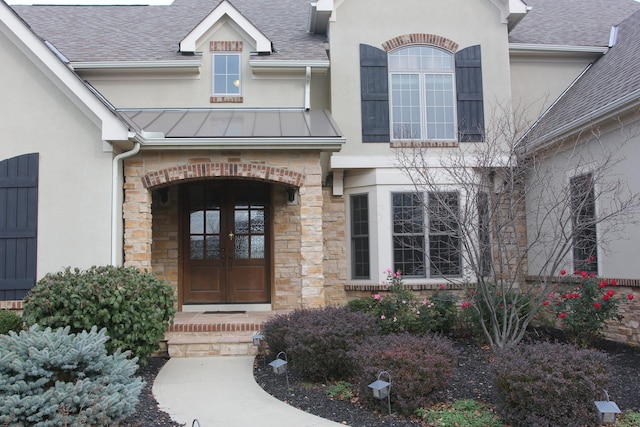 6884 Ballantrae Pl, Dublin, OH 43016 - view of exterior entry featuring stucco siding, a standing seam roof, stone siding, french doors, and roof with shingles