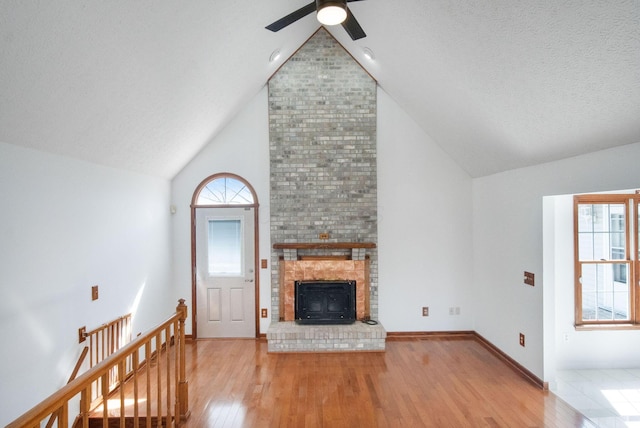 unfurnished living room featuring baseboards, a fireplace, wood finished floors, high vaulted ceiling, and a ceiling fan