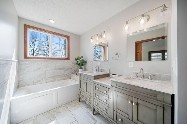 bathroom featuring a sink, a textured ceiling, a bath, and double vanity