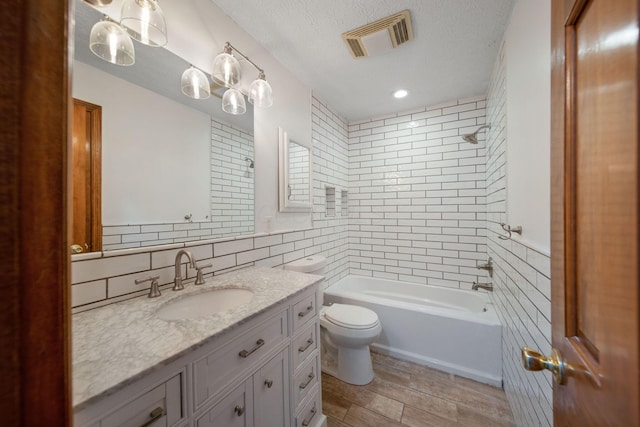 full bathroom with visible vents, toilet, a textured ceiling, tile walls, and vanity