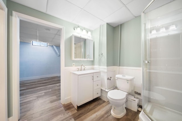 bathroom with toilet, a drop ceiling, wood finished floors, a shower stall, and wainscoting