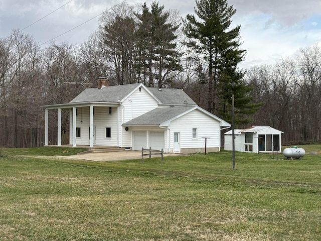 rear view of property with a lawn, a garage, driveway, and a chimney