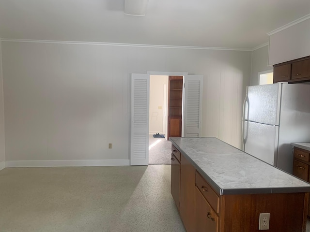 kitchen featuring ornamental molding, light speckled floor, a center island, freestanding refrigerator, and baseboards