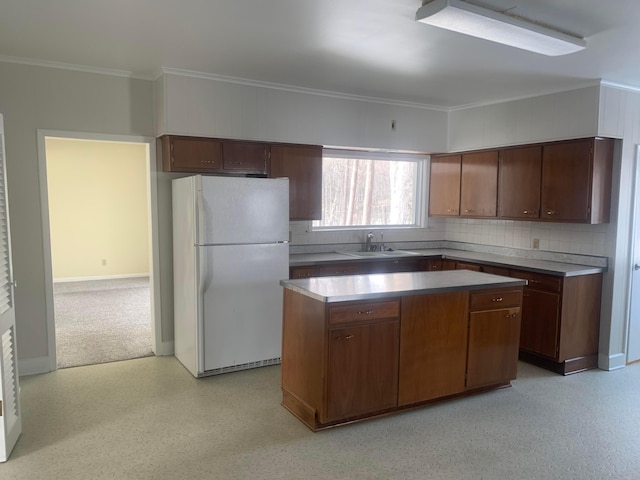 kitchen with a sink, backsplash, a kitchen island, freestanding refrigerator, and crown molding