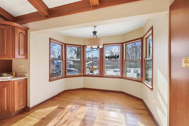 unfurnished dining area featuring light wood-style flooring, beamed ceiling, baseboards, and a chandelier