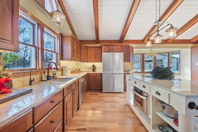 kitchen featuring light wood finished floors, a sink, hanging light fixtures, appliances with stainless steel finishes, and backsplash