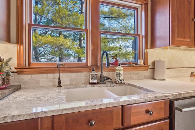 kitchen featuring light stone countertops, a sink, tasteful backsplash, brown cabinets, and a wealth of natural light