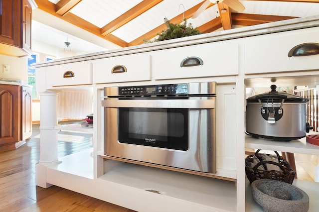 kitchen featuring oven, light wood-style floors, and vaulted ceiling with beams