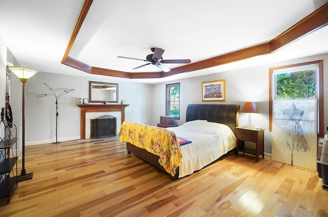 bedroom featuring a fireplace, a raised ceiling, wood finished floors, and baseboards