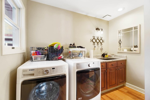 clothes washing area with independent washer and dryer, baseboards, cabinet space, a sink, and light wood-type flooring