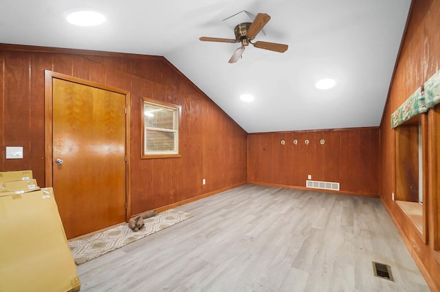 bonus room featuring wooden walls, visible vents, ceiling fan, lofted ceiling, and light wood-style flooring