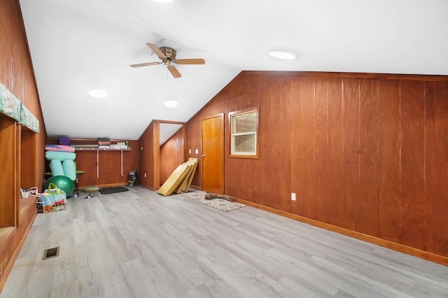 additional living space featuring vaulted ceiling, wooden walls, wood finished floors, and a ceiling fan