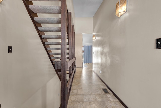 corridor featuring visible vents, baseboards, stairs, and stone finish floor