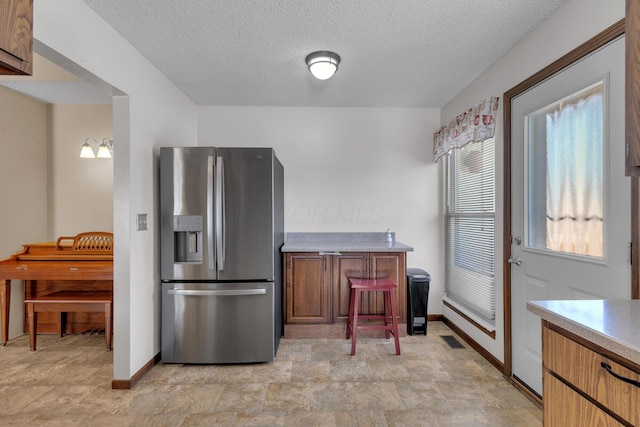 kitchen featuring visible vents, a textured ceiling, stainless steel fridge, brown cabinetry, and light countertops