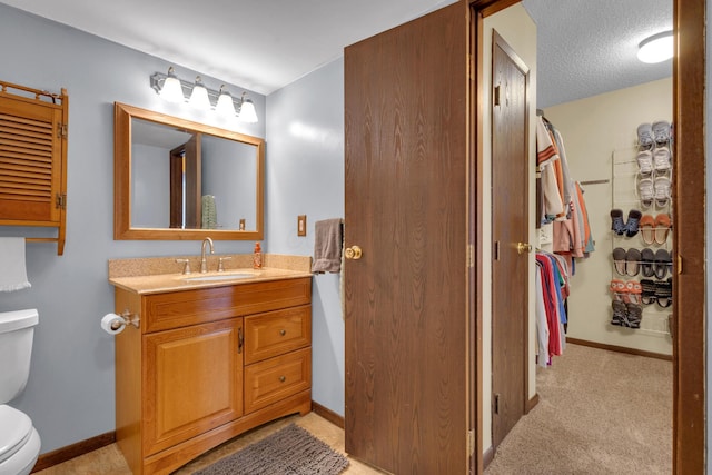 bathroom with baseboards, toilet, vanity, a closet, and a textured ceiling