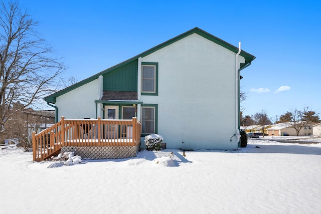 snow covered back of property with stucco siding and a wooden deck