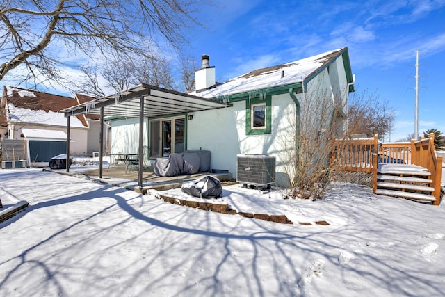 snow covered rear of property with central air condition unit, a wooden deck, a chimney, a storage shed, and an outbuilding