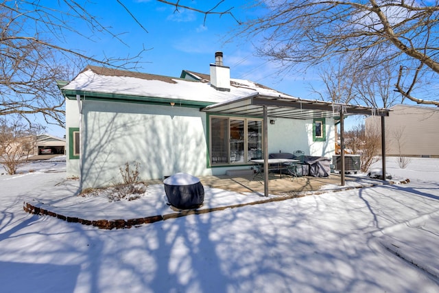 snow covered property featuring stucco siding, a chimney, and a patio area