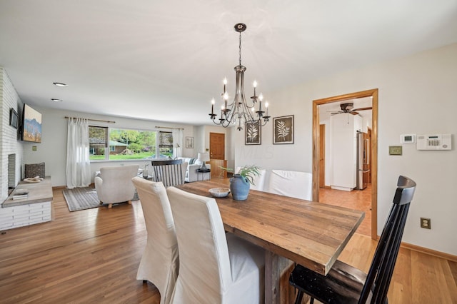 dining area featuring a fireplace, baseboards, wood finished floors, and ceiling fan with notable chandelier