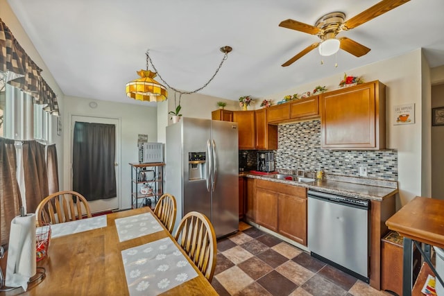 kitchen featuring brown cabinetry, a ceiling fan, a sink, decorative backsplash, and appliances with stainless steel finishes