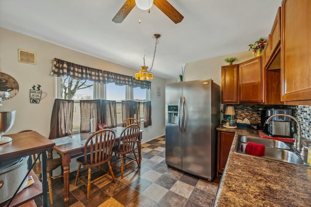 kitchen featuring a sink, backsplash, stainless steel fridge, brown cabinetry, and ceiling fan