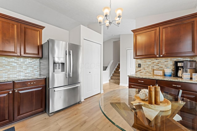 kitchen with stainless steel fridge, light wood finished floors, tasteful backsplash, a chandelier, and light stone counters