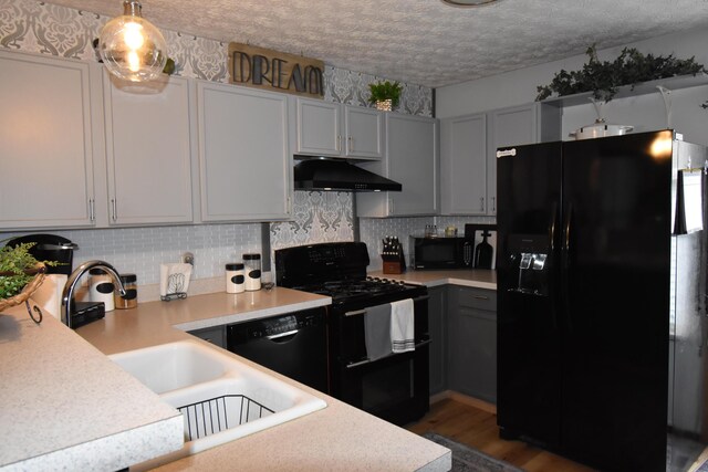 kitchen with backsplash, black appliances, under cabinet range hood, light countertops, and a textured ceiling