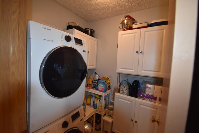 clothes washing area featuring a textured ceiling, cabinet space, and stacked washing maching and dryer