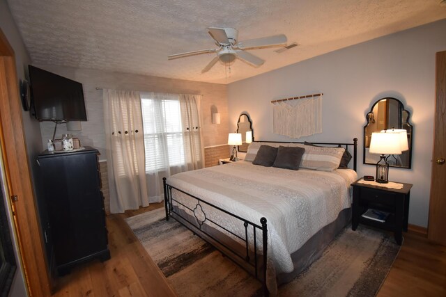 bedroom with visible vents, a textured ceiling, wood finished floors, and a ceiling fan