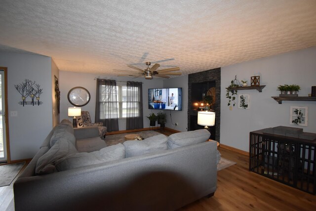 living area with baseboards, a textured ceiling, ceiling fan, and wood finished floors
