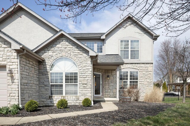 view of front of house with stone siding, fence, a garage, roof with shingles, and stucco siding