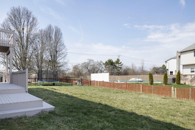 view of yard featuring a trampoline, fence, and a deck