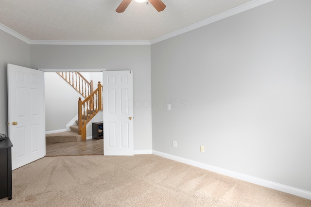 unfurnished room with carpet flooring, crown molding, baseboards, stairway, and a ceiling fan