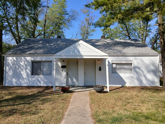 view of front facade featuring a front yard, a chimney, and a shingled roof