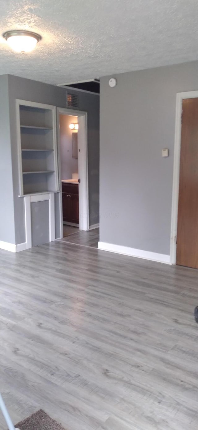 unfurnished living room with visible vents, wood finished floors, baseboards, and a textured ceiling