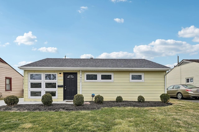 view of front facade featuring a shingled roof and a front yard