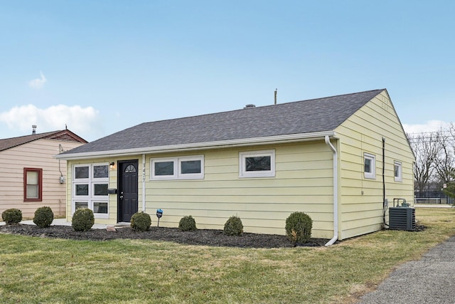 view of front of home featuring central AC, a front lawn, and a shingled roof