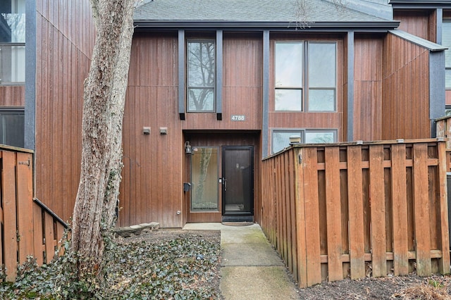 entrance to property featuring a shingled roof and fence