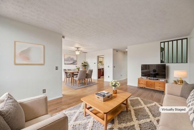 living area featuring baseboards, a ceiling fan, light wood-type flooring, and a textured ceiling